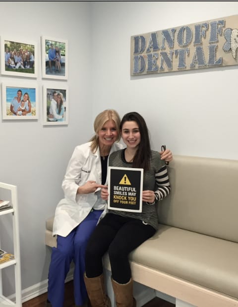 Dr. Danoff sitting with girl that is holding a sign that says beautiful smiles may knock you off your feet