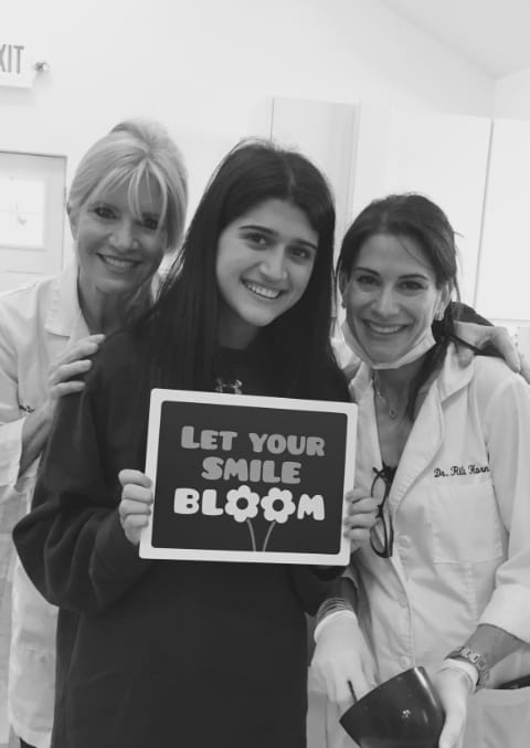 Dr. Danoff and Dr. Fromer posing with teenage girl holding a sign that says let your smile bloom