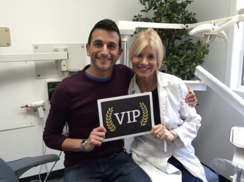 Dr. Danoff sitting on dental chair with man hoolding a sign that says VIP