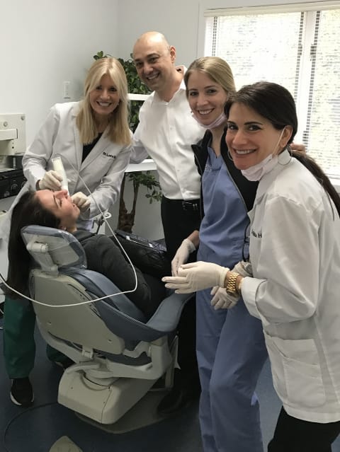 Group of people gathered around dental chair looking at camera while Dr. Danoff scans the mouth of the patient in the chair